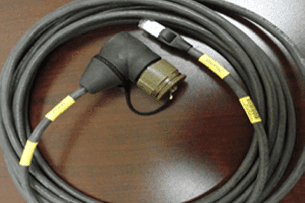 A coiled black cable with a round connector on a wooden surface.